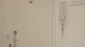 A WC with a green 'GO' sign and a red 'STOP' sign, a white door, and a wall-mounted electrical box. - ABAI Hostel (Vienna)