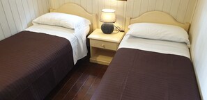 A room with two single beds, each with a white pillow and a brown bedspread. There is a bedside table with a lamp between the beds.