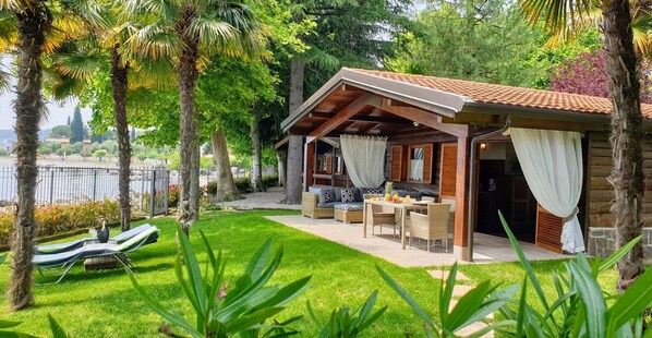 A cozy outdoor seating area with a table and chairs, surrounded by lush greenery and a view of a body of water.