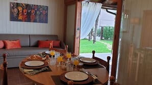 A dining area with a table set for breakfast, a sofa with cushions, and a painting of spices on the wall.