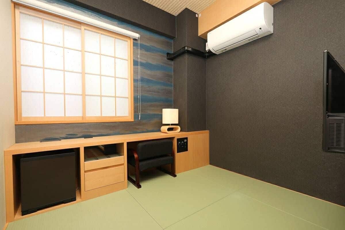 A room with a sliding shoji screen window, a desk with a lamp, a small cabinet, and an air conditioning unit.