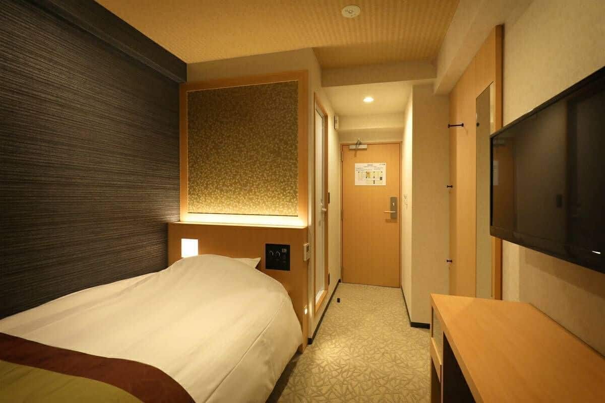 A hotel room with a bed, a television, a wooden desk, and a patterned wall.