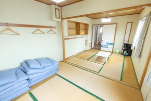 A traditional Japanese room with tatami flooring, a bed with blue bedding, a television, and a mirror. - Kame Kame House (Tokashiki)