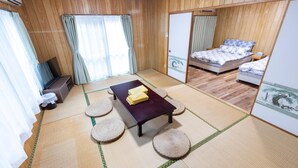 Een traditionele Japanse kamer met tatami vloeren, een futonbed, een klein tafeltje met kussen, en een schuifdeur die leidt naar een andere kamer.