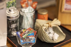 A glass bowl containing colorful packaged items, a metal container, a woven bag, and a small basket on a tray.