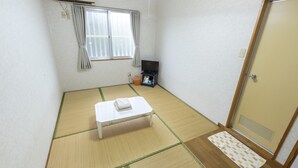 Een kleine, eenvoudig ingerichte kamer met tatami vloerbedekking, een enkel bed, een televisie en een schuifdeur.