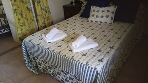 A neatly made bed with a patterned bedspread and pillows, two rolled towels on the bed, and a nightstand with a lamp and a telephone. - Salvador's barrack (Canyadora)