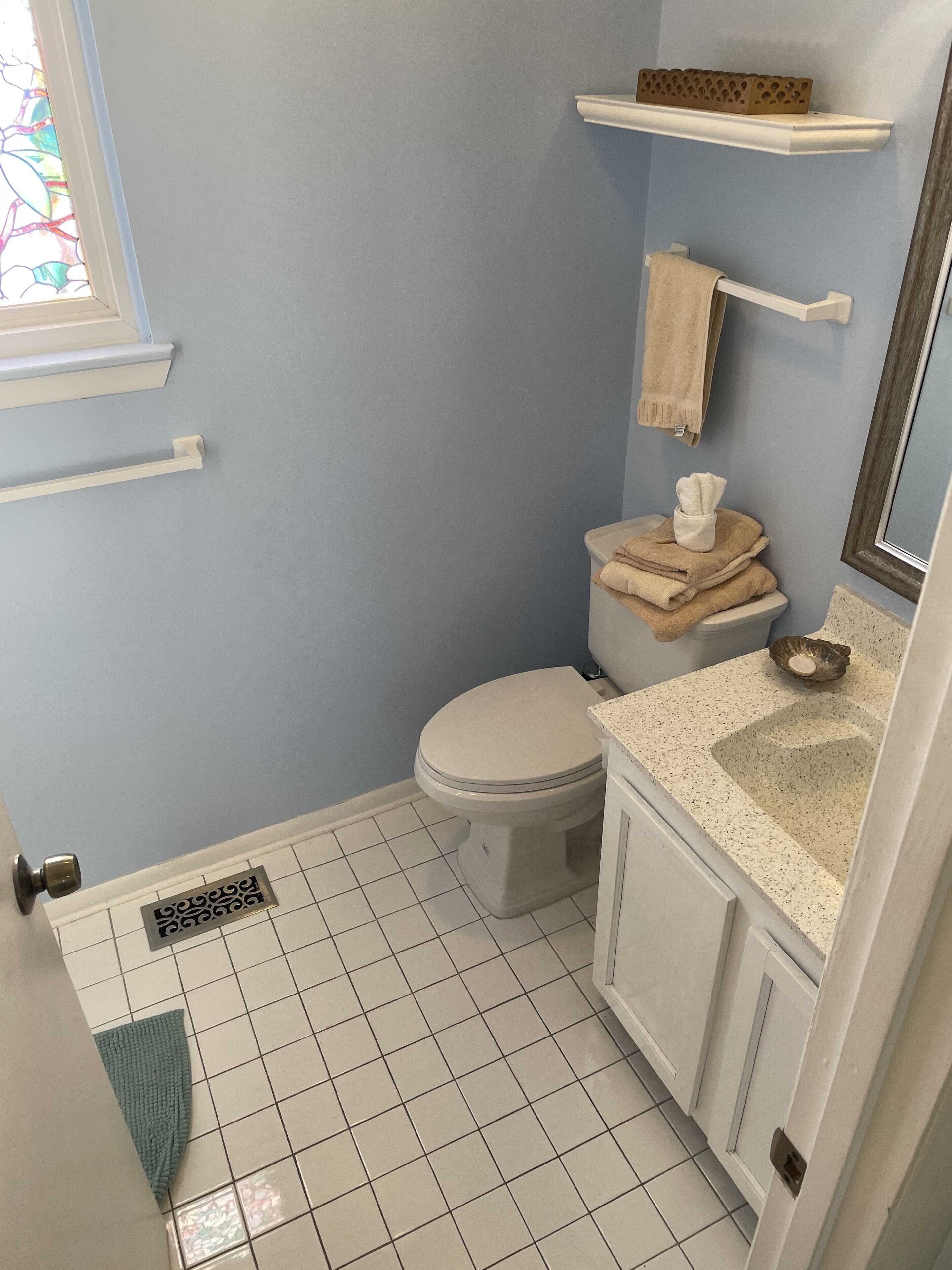 A bathroom with a white toilet, a sink with a speckled countertop, a blue wall, and a window with a stained glass design.