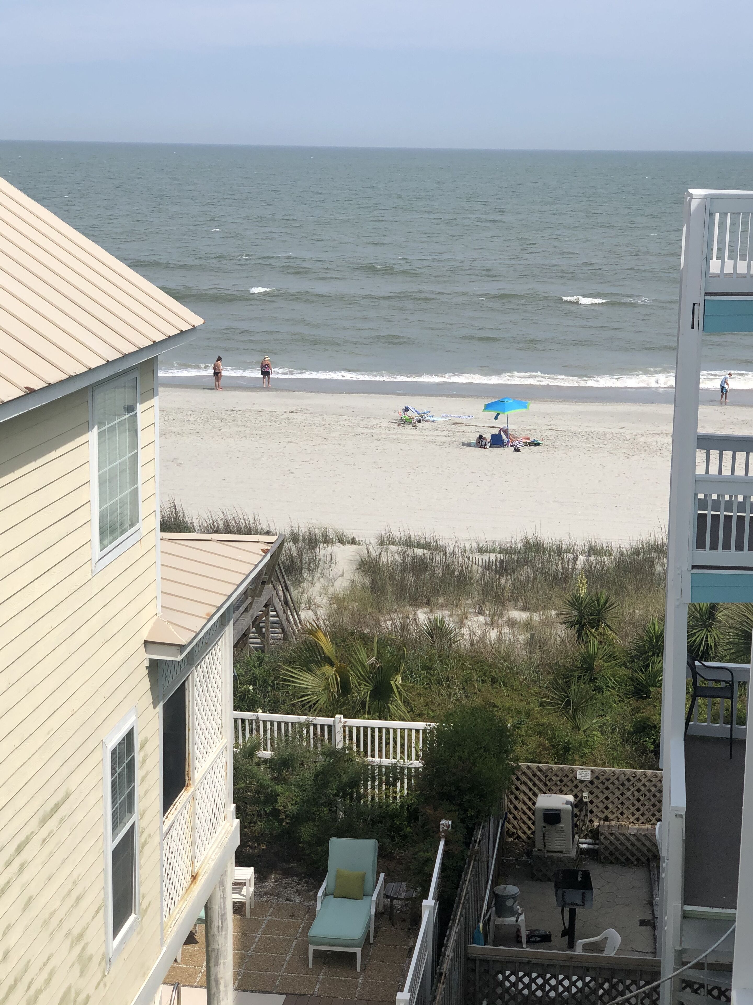 A beach view from a balcony overlooking a sandy beach with a few people and beach chairs.