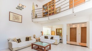 A spacious living area with a high ceiling, a glass coffee table, two white sofas, and a wooden staircase leading to an upper level. - Aeonian Mansion (Zakynthos)