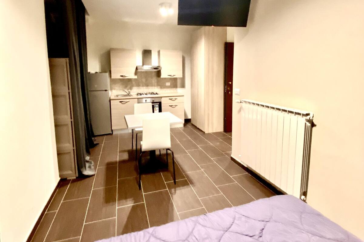 Ein kompaktes Hotelzimmer mit Bett, einer Küchenzeile und einem an der Wand befestigten Fernseher.