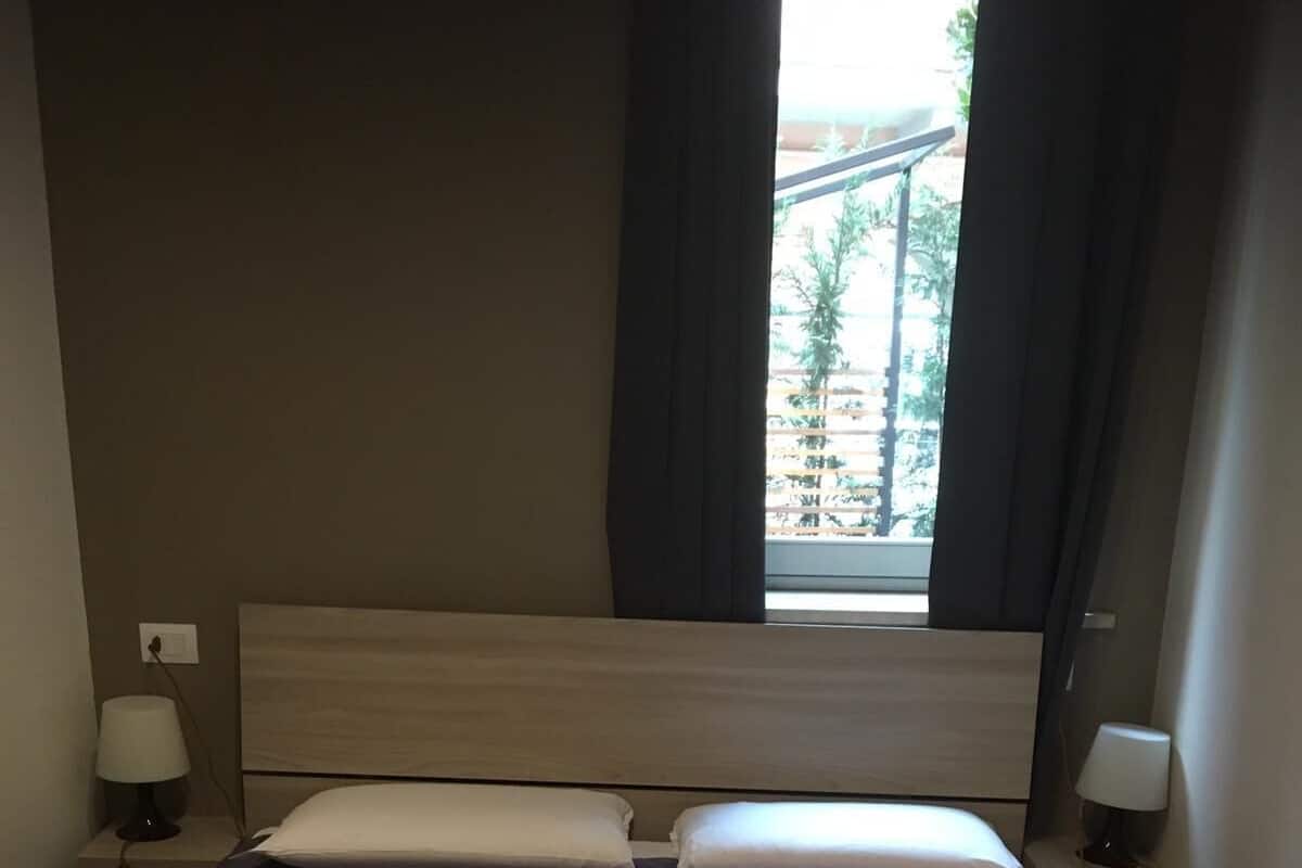 Ein ordentlich bezogenes Bett mit einer violetten Steudecke, zwei Kissen und einer Fernbedienung auf einem gefalteten Handtuch.