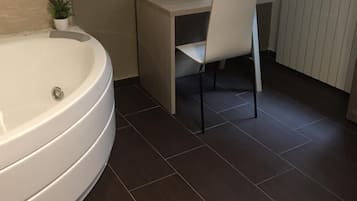 A modern bathroom with a large bathtub, a small desk with a chair, and a potted plant.