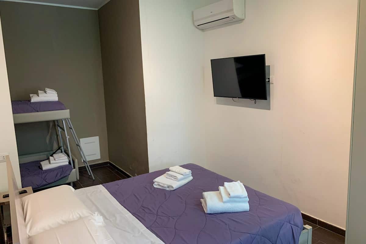 Ein Hotelzimmer mit einem Einzelbett, einem an der Wand befestigten Fernseher und einem Stockbett in der Ecke.