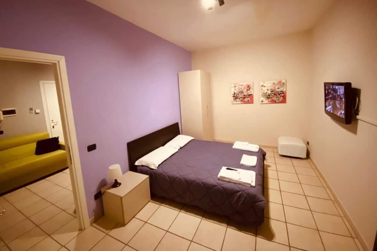 Ein Schlafzimmer mit einem Bett, einem Nachttisch, einer Lampe, einem Fernseher und Bildern an der Wand.
