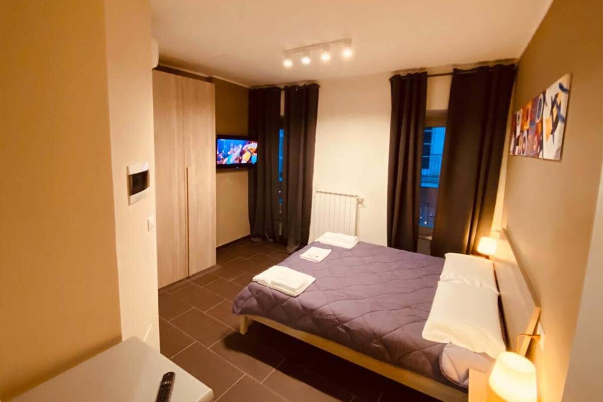 Ein Hotelzimmer mit Bett, Fernseher, Schreibtisch und einem fenster mit Vorhängen.
