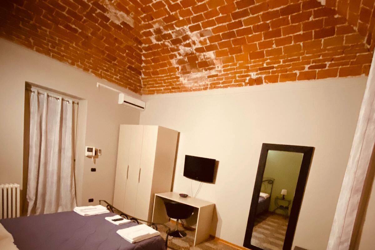 Ein Zimmer mit Ziegeldecke, einem Bett, einem Schreibtisch, einem Spiegel und einem Heizkörper.