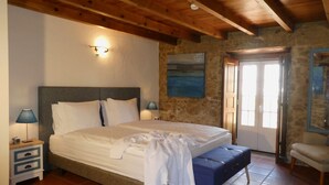 A bedroom with a large bed, wooden ceiling beams, stone walls, a nightstand with a lamp, and a bench. - Vida-Vi, Country House and B&B (Caldas da Rainha)