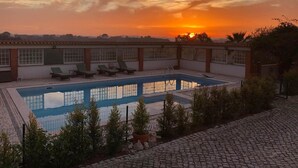 A rectangular swimming pool with a tiled deck, surrounded by a low brick wall. There are several lounge chairs aligned along the wall, and a small section of greenery is visible in the foreground. - Vida-Vi, Country House and B&B (Caldas da Rainha)