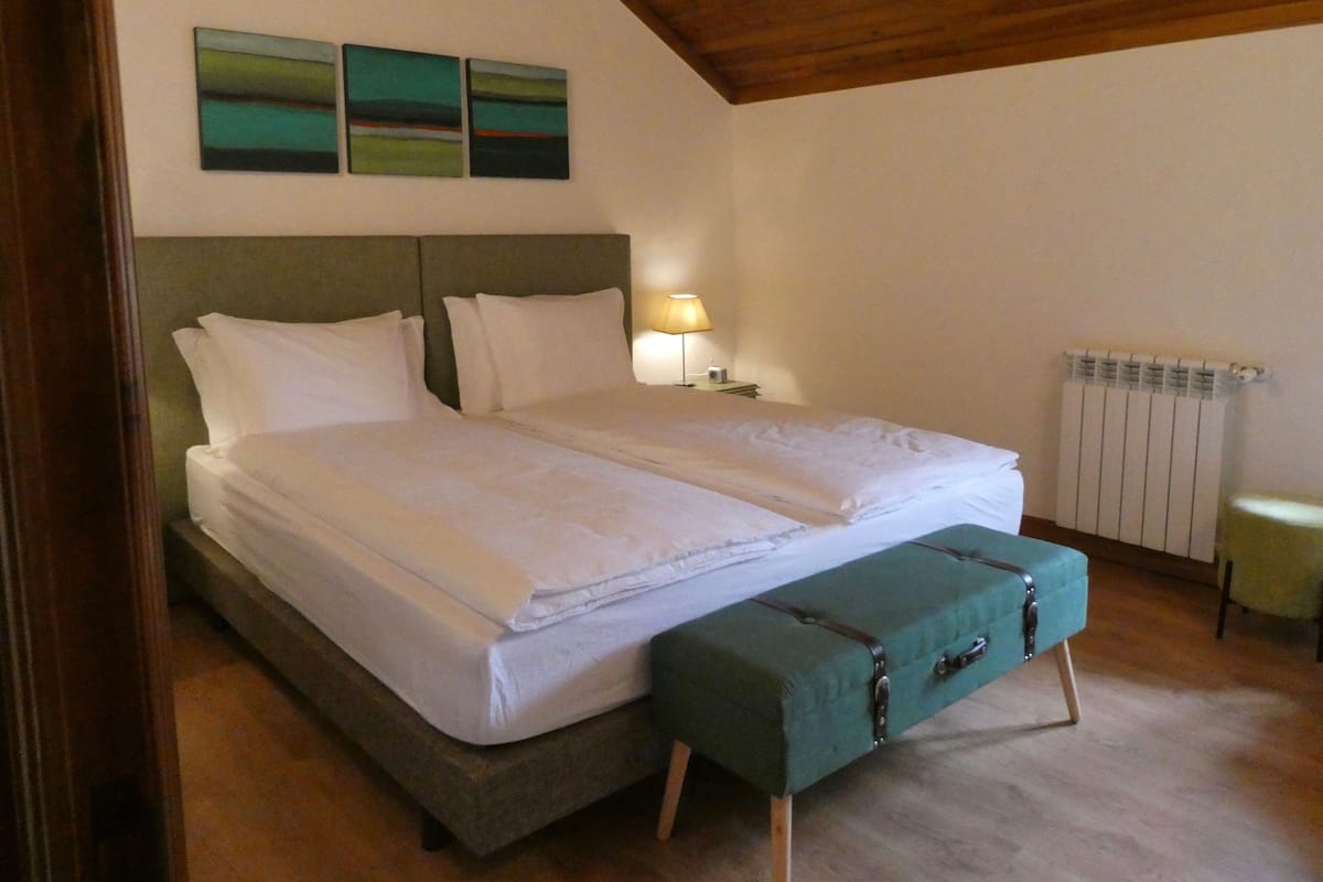 A double bed with a bench, a bedside table with a lamp, and three paintings on the wall.
