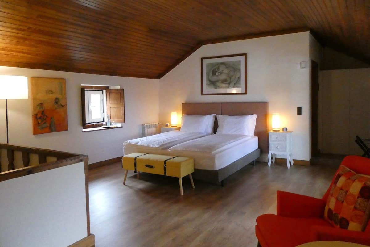 A bedroom with a wooden ceiling, a bed with white bedding, a red chair, and a small table with a lamp.
