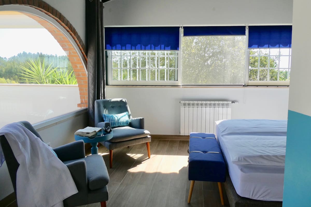 A room with a bed, a chair, a table, and a window with blue curtains.