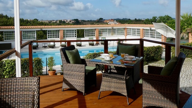 A terrace with wicker furniture, a table with cups and a glass, and a view of a swimming pool and buildings in the background. - Vida-Vi, Country House and B&B (Caldas da Rainha)