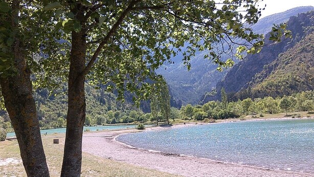 Une rivière bordée d’une plage de galets, entourée d’arbres et de montagnes.