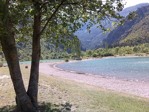 Une rivière bordée d’une plage de galets, entourée d’arbres et de montagnes.