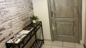 Ein Korridor mit Backsteinwand, einer Holztür und einem Konsolentisch mit Blumentopf und Broschüre.