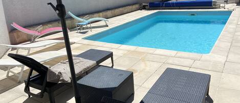 A swimming pool with lounge chairs and a sunshade.