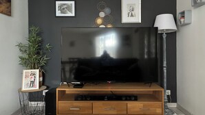 Ein Flachbildfernseher an einer Holztruhe, mit einer Lampe und gerahmten Bildern an der Wand.