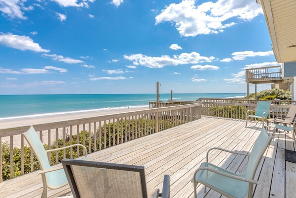 Una terraza de madera con sillas que da a una playa.