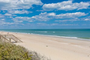 A beach with a wooden walkway leading to the water, a clear sky, and calm sea.