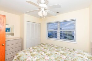 Une chambre à coucher comprenant un lit, un ventilateur de plafond, une fenêtre avec des stores, une commode et un placard.