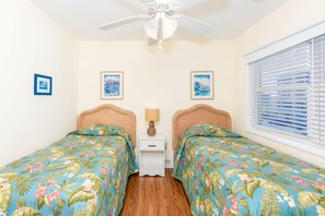 A bedroom with two single beds, a ceiling fan, a nightstand with a lamp, and two framed pictures on the wall.