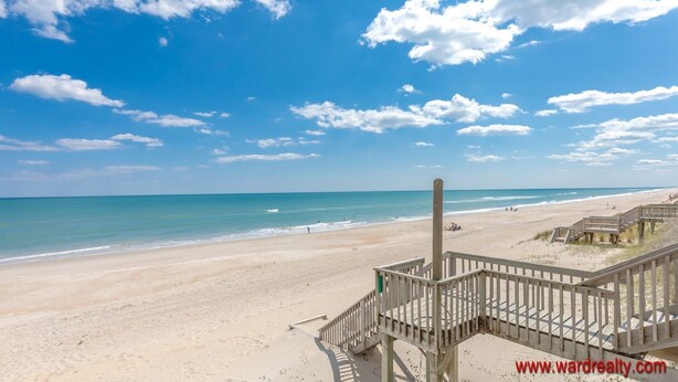 A beach with a wooden boardwalk leading to a structure, clear skies, and calm sea. - Periwinkle - Oceanfront 3 BR, 2.5 BA home in Surf City!  Dog Friendly! (Surf City)
