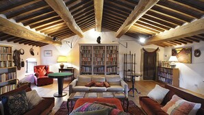 A cozy living room with a high wooden ceiling, a fireplace, and a large bookshelf filled with books. - Medieval Tuscan Castle  with 8 bedrooms for 18 guests (Seggiano)