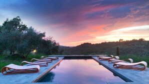 A rectangular pool with lounge chairs on either side, surrounded by greenery and a sunset view. - Medieval Tuscan Castle  with 8 bedrooms for 18 guests (Seggiano)