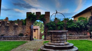An ancient stone archway leading to a courtyard with a fountain and a rustic building in the background. - Medieval Tuscan Castle  with 8 bedrooms for 18 guests (Seggiano)