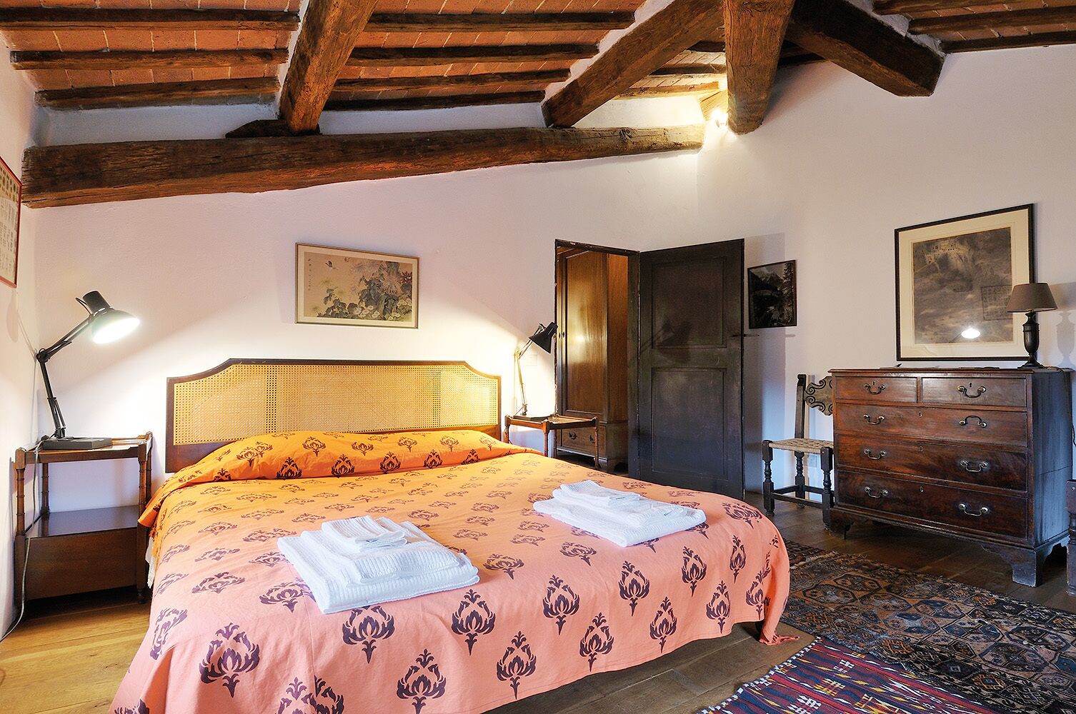 A bedroom with a bed, wooden headboard, bedside tables with lamps, a dresser, and a door.