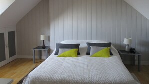 A bedroom with a sloped ceiling, a bed with white bedding and two pillows, two bedside tables with lamps, and a wooden floor. - HOUSE NEAR ROSAIRES BEACH (Plérin)