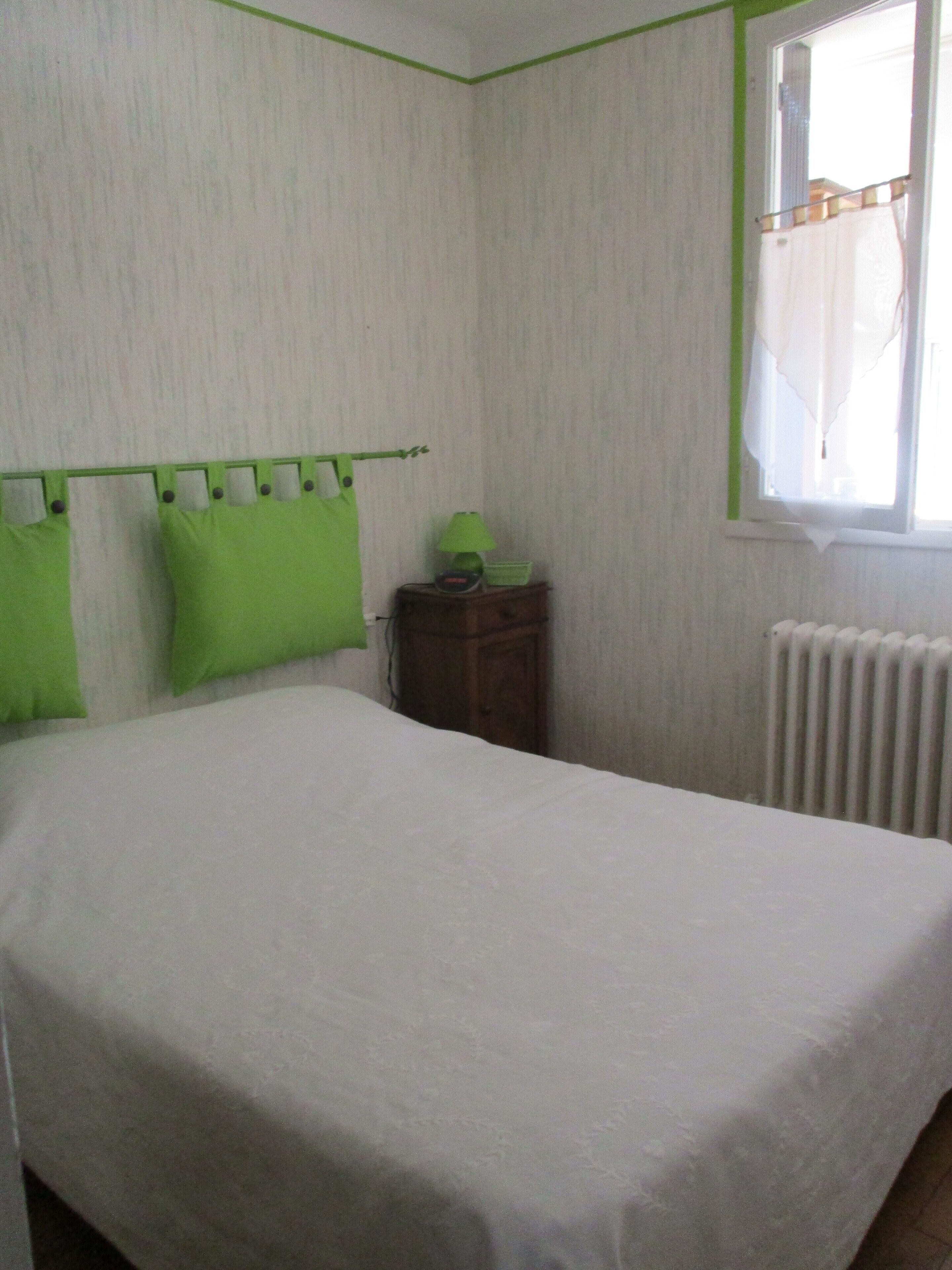 A bedroom with a bed, a nightstand, a lamp, and a window with curtains.