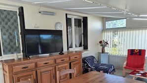 A dining area with a wooden table, chairs, a television, and a clock on the wall. - HOUSE NEAR ROSAIRES BEACH (Plérin)