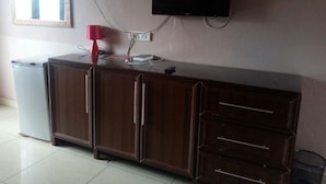 A room with a wooden cabinet, a television mounted on the wall, a red lamp, and a trash bin. - Starscape Hotel (Ndola)