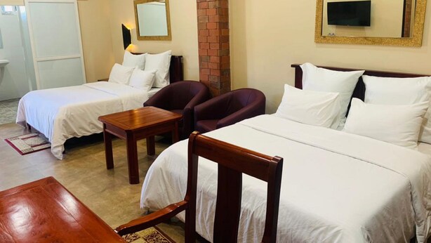 A hotel room with two single beds, a wooden table, a chair, a TV, and a brick wall. - Starscape Hotel (Ndola)