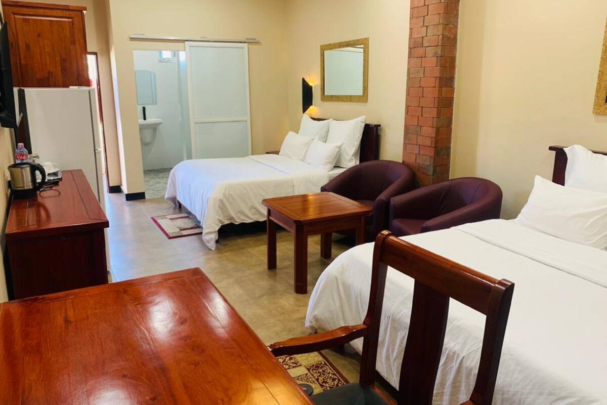 A hotel room with two single beds, a wooden table, a desk with a telephone, and a brick wall.