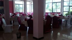 A spacious indoor area with multiple tables and chairs, large windows allowing natural light, and a tiled floor. - Starscape Hotel (Ndola)