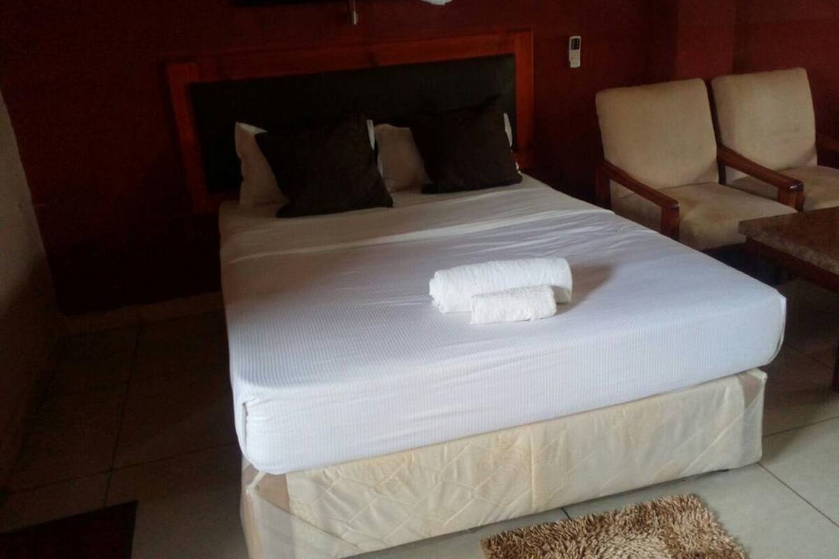 A hotel room with a large bed, two pillows, a headboard, a chair, and a small table.