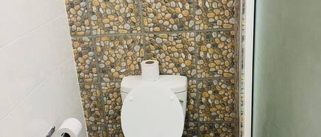 A bathroom with a white toilet, stone-patterned walls, and a tiled floor.
